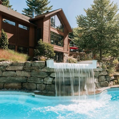 Chute thermale en pierre se déversant dans une piscine à l'Amerispa Spa Nordique Morin-Heights en été.