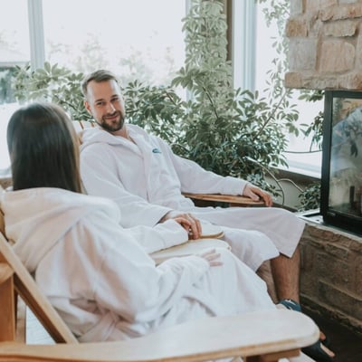 Couple en peignoir se détendant devant le foyer dans une aire de repos de l'Amerispa Morin-Heights.