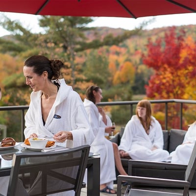 Groupe d'amies en peignoir partageant un repas sur la terrasse de l'Amerispa Morin-Heights avec vue sur les couleurs d'automne.