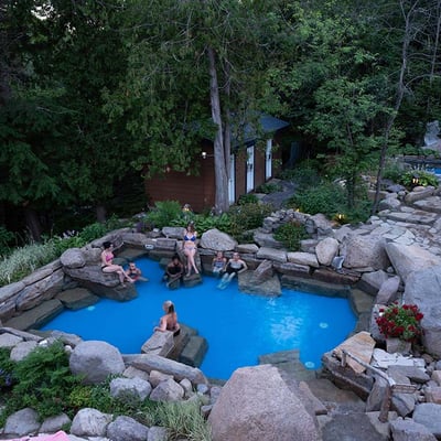 Groupe se relaxant dans le bassin nordique de l'Auberge & Spa Beaux Rêves en soirée, avec un éclairage doux créant une atmosphère intime.