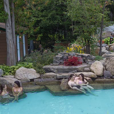 Groupes d'amis se relaxant dans les bains extérieurs en pierre de l'Auberge & Spa Beaux Rêves, avec une chute en arrière-plan.