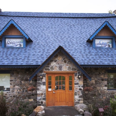 Façade du bâtiment du spa de l'Auberge & Spa Beaux Rêves, une charmante maisonnette en pierre avec un toit bleu et une porte en bois.