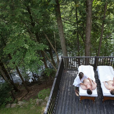 Couple recevant un massage en duo sur une terrasse extérieure privée, surplombant la rivière aux Mulets à l'Auberge & Spa Beaux Rêves.