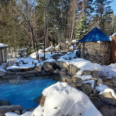 Vue des installations du spa de l'Auberge & Spa Beaux Rêves en hiver, avec les bains chauds fumants entourés de neige.