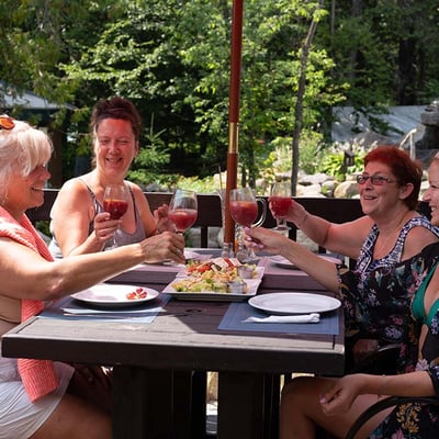 Groupe de femmes souriantes trinquant avec des verres de sangria sur la terrasse de l'Auberge & Spa Beaux Rêves, partageant un repas en été.