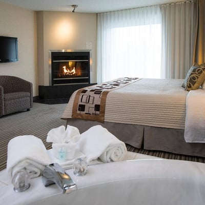 Chambre confortable à l'Excelsior Hôtel Spa, mettant en vedette un foyer allumé et un bain tourbillon au premier plan.
