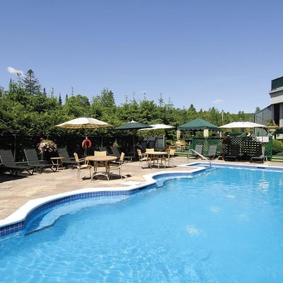 La grande piscine extérieure de l'Excelsior Hôtel Spa à Sainte-Adèle, entourée de chaises longues et de parasols lors d'une journée ensoleillée.
