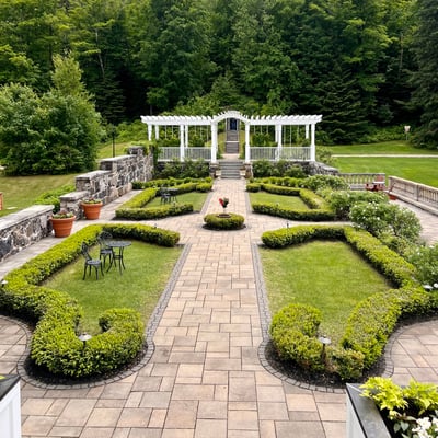 Jardin du Spa StoneHaven Le Manoir avec allées pavées, arbustes taillés et gloriette blanche.