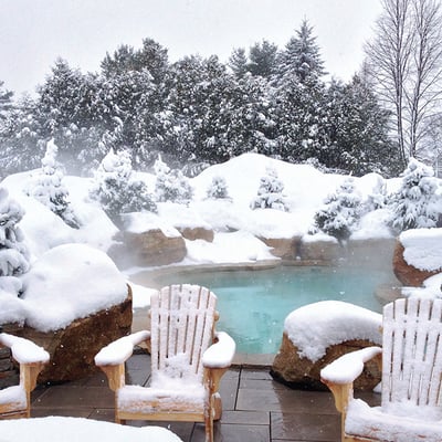 La piscine extérieure chauffée du Manoir Saint-Sauveur entourée d'un paysage enneigé, offrant une expérience magique en hiver.