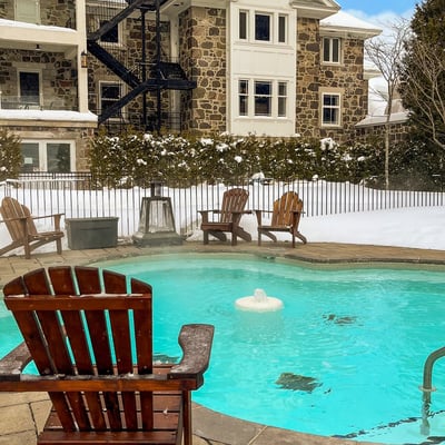 Piscine extérieure chauffée du Spa StoneHaven Le Manoir entourée de neige et de fauteuils Adirondack.