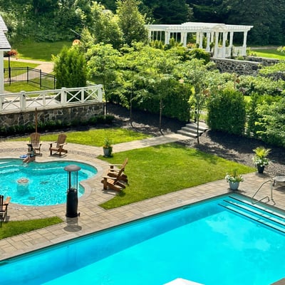 Piscine extérieure et bain tourbillon du Spa StoneHaven Le Manoir entourés de verdure et de chaises en bois.