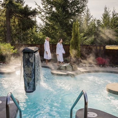 Couple en peignoir se promenant près des bains thermiques et d'une chute en pierre au Scandinave Spa Mont-Tremblant.