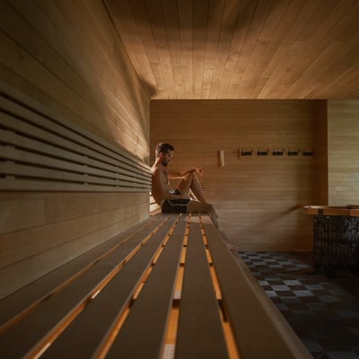 Homme se relaxant seul dans le grand sauna finlandais en bois du Scandinave Spa, avec une fenêtre donnant sur la forêt.