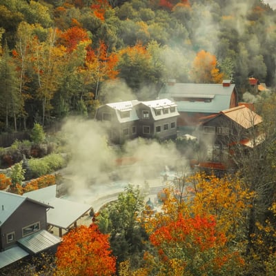 Vue aérienne du complexe Scandinave Spa à Mont-Tremblant, avec la vapeur des bains s'élevant au milieu des arbres aux couleurs d'automne.