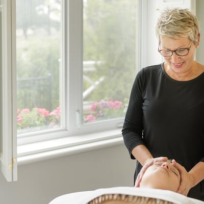 Esthéticienne réalisant un soin du visage au Spa StoneHaven Le Manoir dans une salle lumineuse avec vue sur les jardins.
