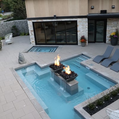Vue plongeante sur l'espace thermal moderne et exclusif du Spa du Manoir, avec sa piscine, ses foyers et ses chaises longues design.