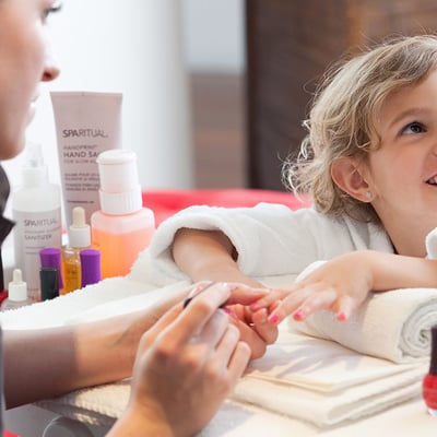 Jeune fille souriante recevant son premier soin de manucure au Spa du Manoir Saint-Sauveur, une offre unique pour les familles.
