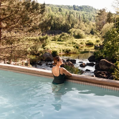 Femme se relaxant dans un bain chaud au Strøm Spa de Saint-Sauveur, avec une vue directe sur la rivière et la nature environnante.