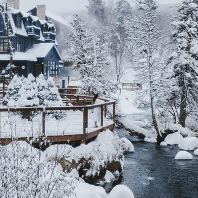 Femme en peignoir sur une terrasse en bois du Strøm Spa à Saint-Sauveur, contemplant le paysage féerique de la rivière sous la neige.