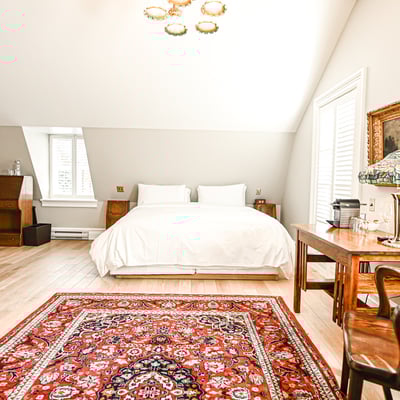 Chambre luxueuse du Spa StoneHaven Le Manoir avec lit blanc, tapis oriental rouge et mobilier ancien.